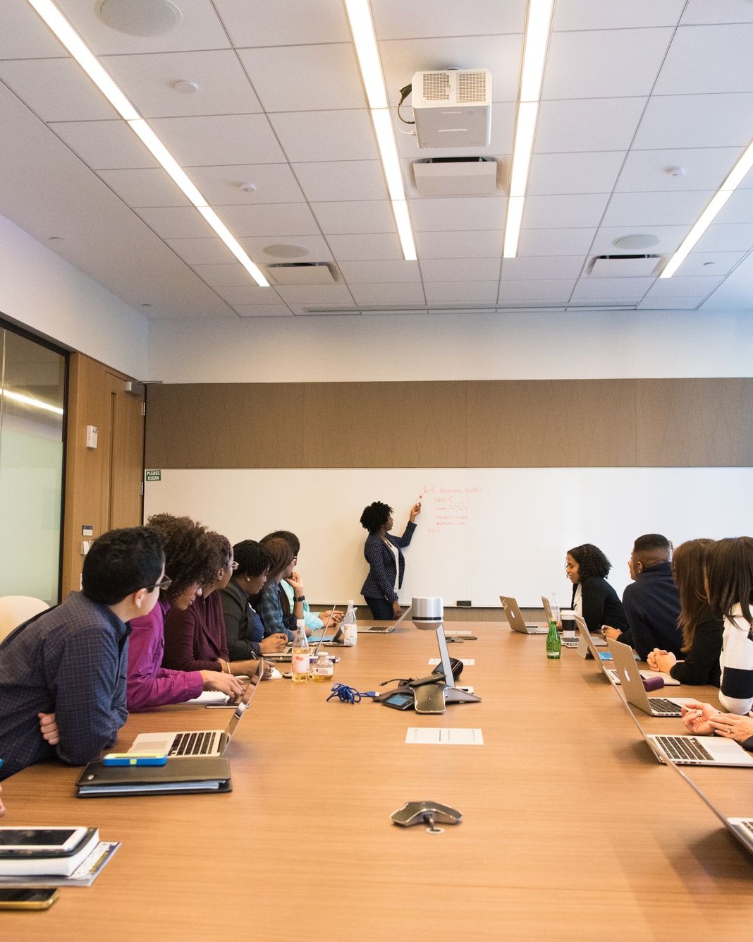 Professionals seated in a training session around a conference table with a facilitator at a whiteboard